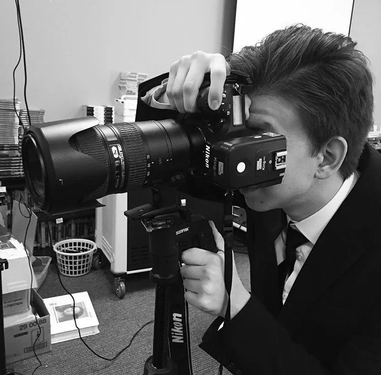 A wedding photographer in Dallas in a suit taking a photograph of newlyweds with a large professional camera on a tripod in an indoor setting.