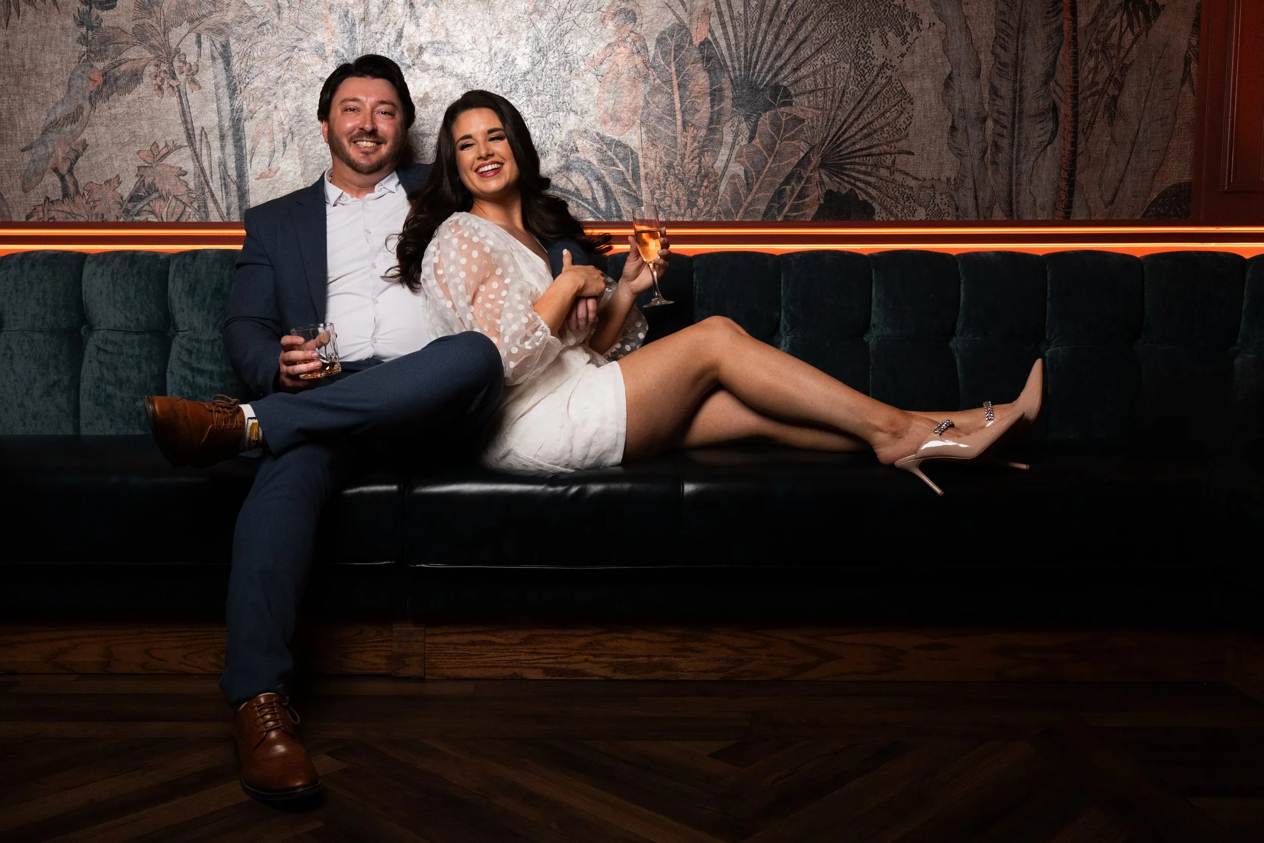 A couple posing for their engagement session on a dark green velvet couch at the Columbia Country Club bar in Dallas