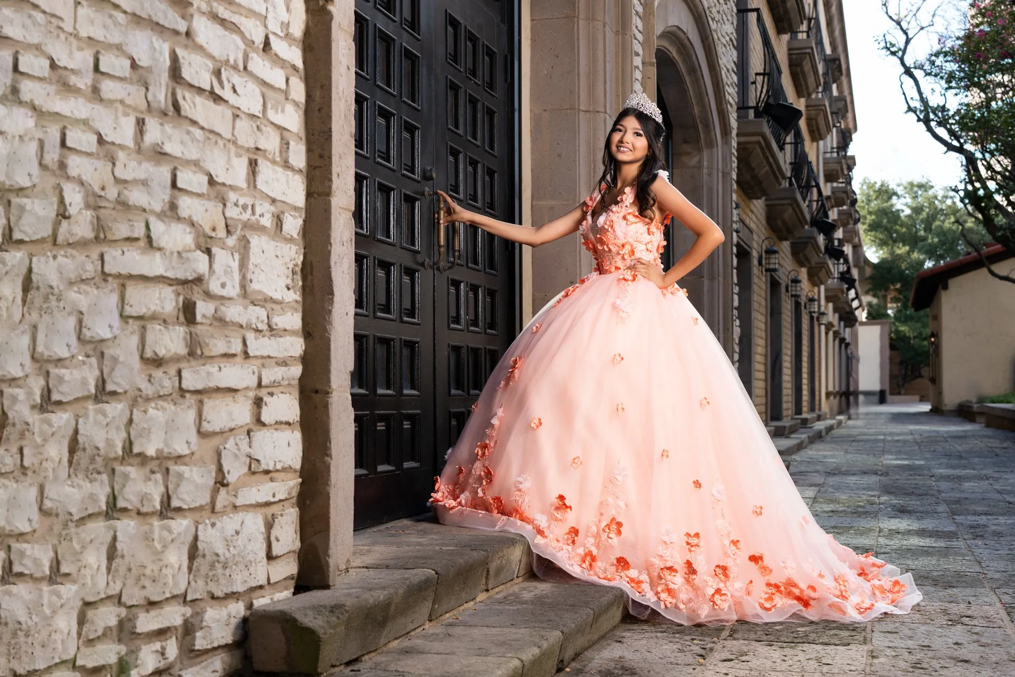 Quinceañera in a peach floral gown posing in front of arched doorway at Mandalay Canal Walk in Las Colinas, Irving, Texas